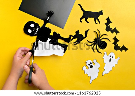 Crafts for Halloween - figures of a spider, bats, ghost and black cat, cut from black and orange paper, scissors, stencils, felt-tip pen, ruler on a yellow background DIY Flat lay Copy space Top view 