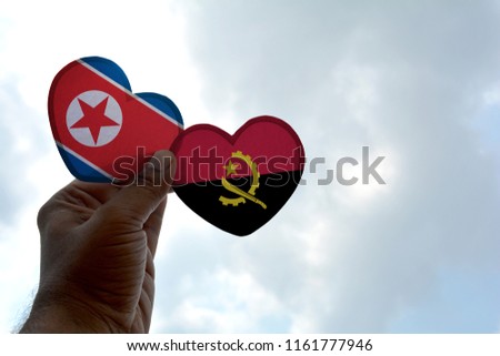 Hand holds a heart Shape North Korea and Angola flag, love between two countries