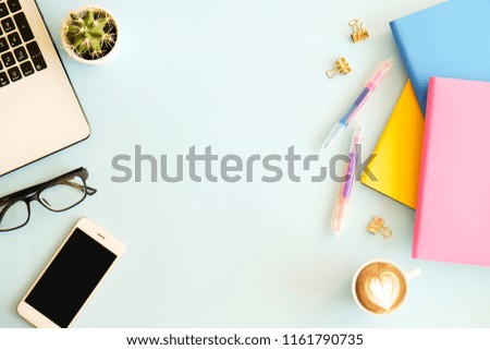 Office workplace with laptop, multiple colorful notebooks, blank screen mobile cell phone, white cup of coffee, supplies and stationery on blue background. Close up, copy space, top view, flat lay.