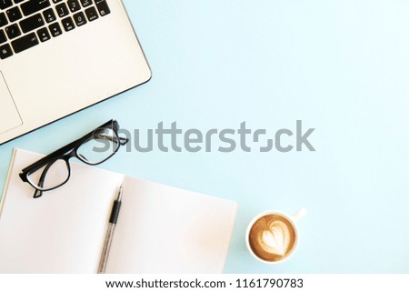 Minimalistic flat lay composition of black & white laptop computer keyboard, cup of coffee & folded glasses, blank pages notebook, pen, blue desk table background. Workspace top view, copy space