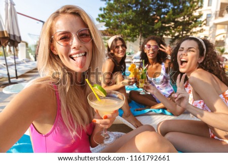 Picture of young happy emotional group of women friends sitting outdoors in pool dressed in swimwears take a selfie by camera.