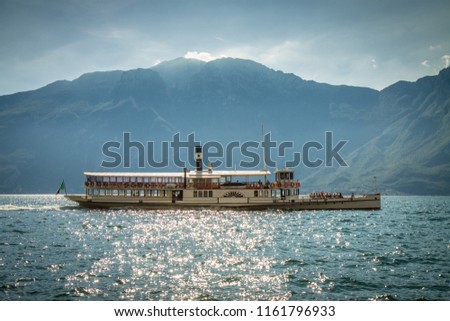 The beautiful view of traditional paddle steam boat floating on the lake Lago di Garda (Limone Sul Garda - Malcesine), Italy. HD background with moutains, blue sky and clouds. Perfect Wallpaper 4k.