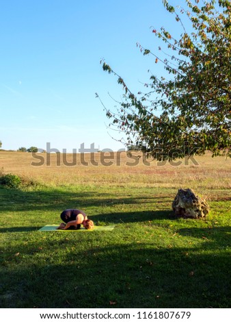 Surrounded by idyllic rural French countryside a mature woman practises her yoga positions in beautiful autumn sunshine. The Child pose.
