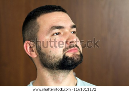 Portrait of handsome bearded confident intelligent modern photogenic young man with short haircut and black eyes looking thoughtfully ahead on blurred background. Youth and confidence concept.
