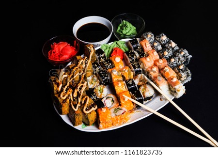 Set of traditional japanese food on a dark background. Sushi rolls, nigiri, raw salmon steak, rice, cream cheese, avocado, lime, pickled ginger. Asian food frame.