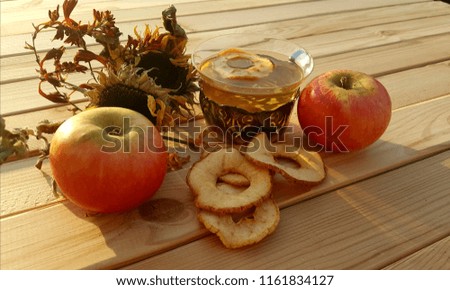A cup of tea from dried apples, dried and fresh apples and dried autumn flowers on a wooden table.