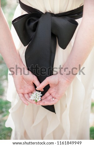 a branch of a blossoming apple tree lies in the hands of a young red-haired bride in the background of a stylish wedding dress with a black bow belt