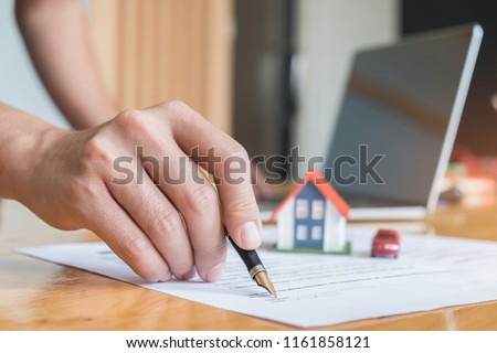 Pen handles signed documents with model houses, model car and laptop on the table.
