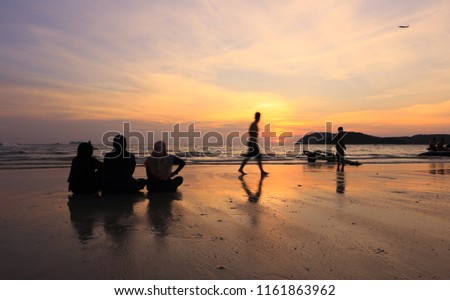 Three women watch the sunset and people on the beach, Langkawi, Malaysia