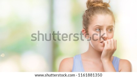 Young blonde woman looking stressed and nervous with hands on mouth biting nails. Anxiety problem.