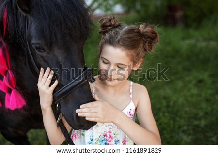 Cute little girl with black pony in the park. Close up picture