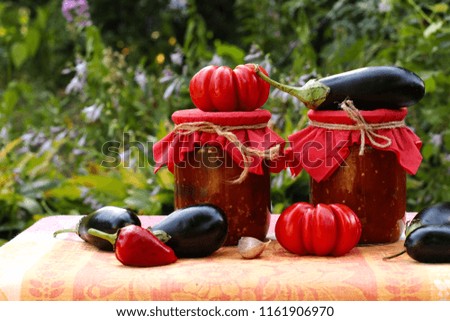 Eggplants in tomatoes in jars are located on a table in the garden, Fresh tomatoes, aubergines, garlic and bell peppers are on the table, blanks for the winter