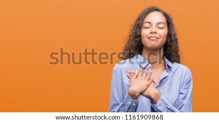 Young hispanic business woman smiling with hands on chest with closed eyes and grateful gesture on face. Health concept.