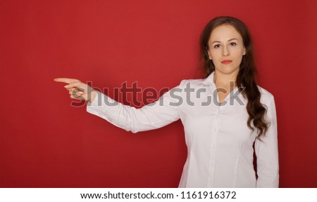 serious woman pointing finger away over red background. Looking at camera
