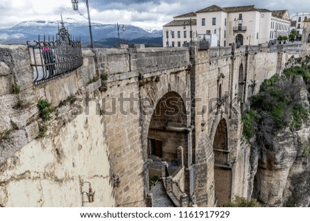New Bridge, (Puente Nuevo) in Ronda with its stone arches and its snowy mountains in the background, on a wonderful cloudy day with a gray sky in the province of Malaga Spain
