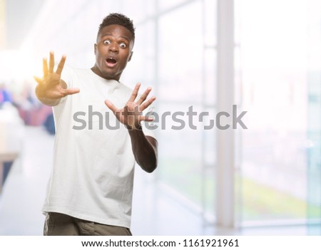 Young african american man wearing white t-shirt afraid and terrified with fear expression stop gesture with hands, shouting in shock. Panic concept.