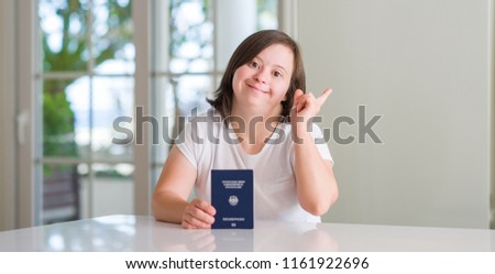 Down syndrome woman at home holding german passport very happy pointing with hand and finger to the side