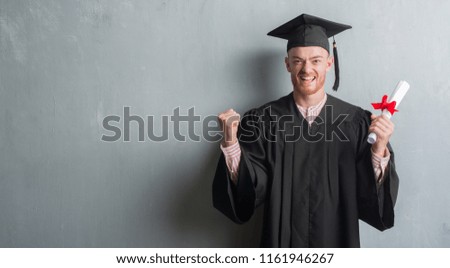 Young redhead man over grey grunge wall wearing graduate uniform holding degree screaming proud and celebrating victory and success very excited, cheering emotion Royalty-Free Stock Photo #1161946267