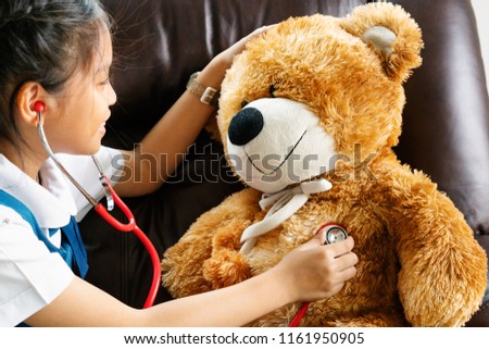 little girl is smiling and playing doctor with brown bear and stethoscope. Kid and health care concept.