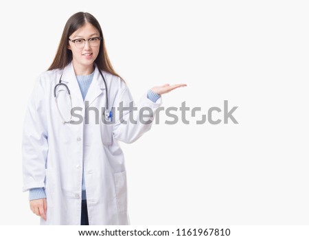 Young Chinese doctor woman over isolated background smiling cheerful presenting and pointing with palm of hand looking at the camera.