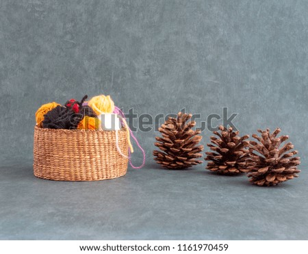 Needlework fall background. With pine cones and colorful balls of wool in a basket. Front view. Yarn for knitting or crochet. 