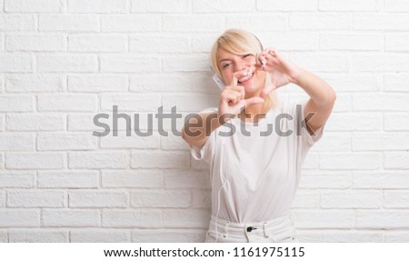 Adult caucasian woman over white brick wall wearing headphones smiling in love showing heart symbol and shape with hands. Romantic concept.
