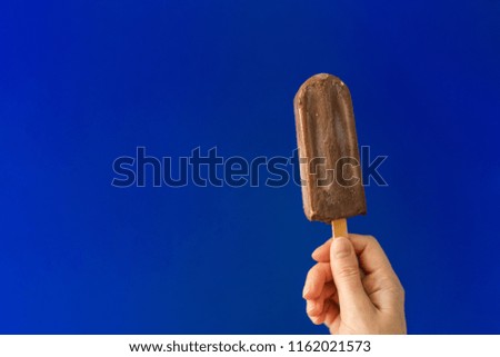 Girl's hand with chocolate ice cream on deep blue background.