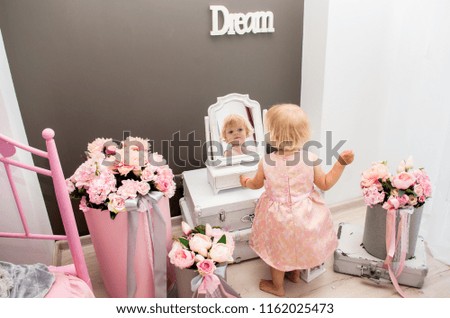 happy blond girl of two years looking in the mirror in a decorated room