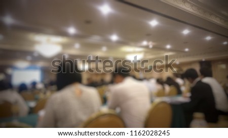 Blurred photo of conference hall or seminar room, people sitting and listening to the host.