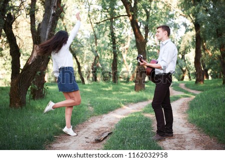 young couple walking in the forest and playing guitar, summer nature, bright sunlight, shadows and green leaves, romantic feelings