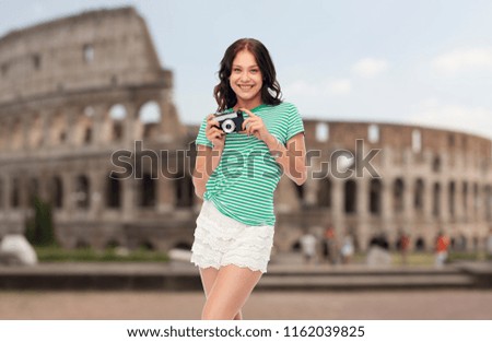 travel, tourism and photography concept - smiling teenage girl with vintage film camera over coliseum background
