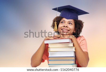 education, school, knowledge and graduation concept - happy smiling african american graduate student girl in mortarboard with books dreaming