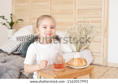 Little blonde girl have a Morning breakfast on wooden tray near bed.