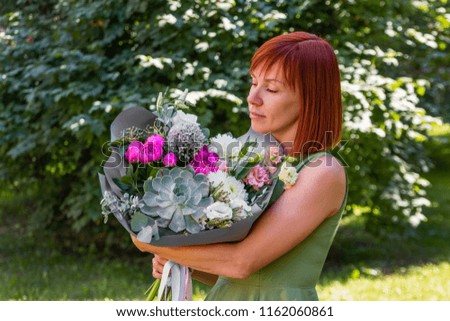 Portrait of beautiful happy red-haired girl who holds a spectacular stylish bouquet of different flowers. Gift from man for his birthday. The concept of the 8th of March, the International Women's day