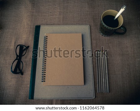 Vintage style. Organized desk with binder, closed notebook, eye glasses, one cup of coffee, pencils and burlap background Royalty-Free Stock Photo #1162064578