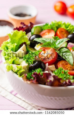 Fresh Greek salad with vegetables, feta cheese and black olives in white bowl on purple wooden background. Selective focus.