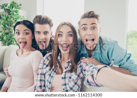 Cute, expression, glad hipsters in stylish casual wear take selfie on the front camera modern smartphone show tongue out