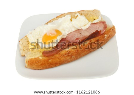 Fried egg and bacon in a crusty roll on a plate isolated against white