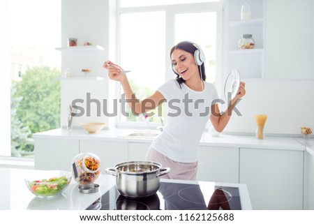 Adorable nice charming cheerful pretty beautiful stylish girl singing, dancing with spoon and pan cover in modern light white kitchen, cooking homemade breakfast dish with domestic products Royalty-Free Stock Photo #1162125688