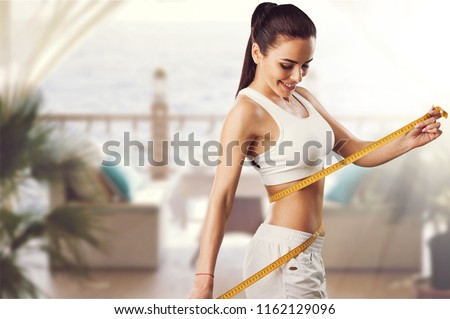 Weight loss, slim body, healthy lifestyle concept. Fit fitness girl measuring her waistline with measure tape on blue Royalty-Free Stock Photo #1162129096