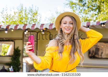 Cheerful girls do selfie on a smartphone on the back of a van in a camping. Road trip with best friends. Adventure, freedom, youth