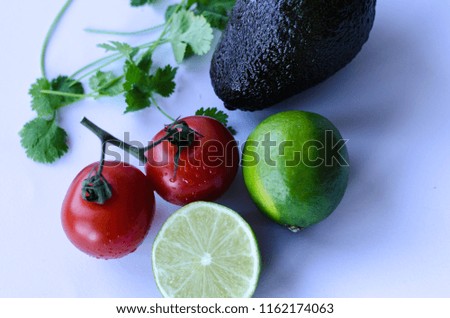 Avocado, lime cut in half, tomatoes on the vine and cilantro/koriander placed in a group on a white background