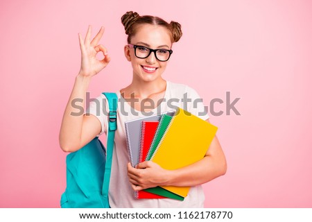Homework is easy! Sweet and cute reader girl shows ok sign holding multicolored notebooks in hands isolated on shine pink background