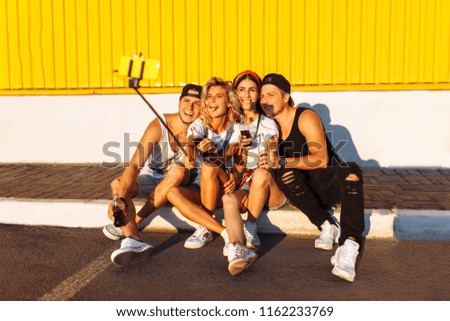 A group of friends makes a selfie sitting on the pavement, the company of young people taking pictures with a selfie stick, cheerful company, Sunny day