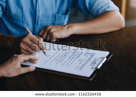 Close up of customer signing a paper document for buying house. Estate agent pointing finger showing where to sign on wooden desk. Agreement and Real estate concept.