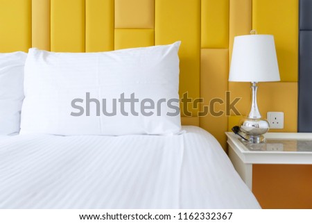 Bed with pillows, lamp and alarm clock in yellow room theme