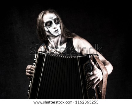 Humorous portrait of man in goth style clothes and scull makeup with the Russian bayan (button accordion).