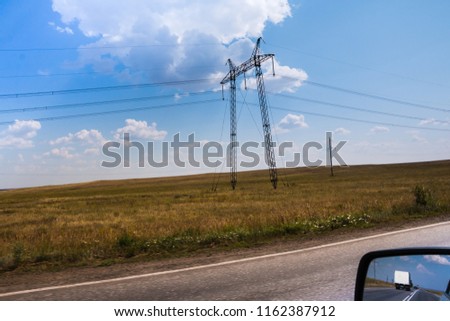 High voltage lines and agricultural landscape on a sunny day with white clouds in the blue sky. Taking photos from a moving car with blurring the edge of the field
