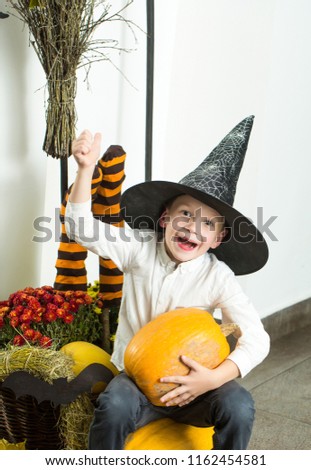 Halloween Small boy in spider web hat at striped socks. Halloween child with happy face. Holiday and celebration. Kid with orange pumpkin in witch hat. Party and traditional food.