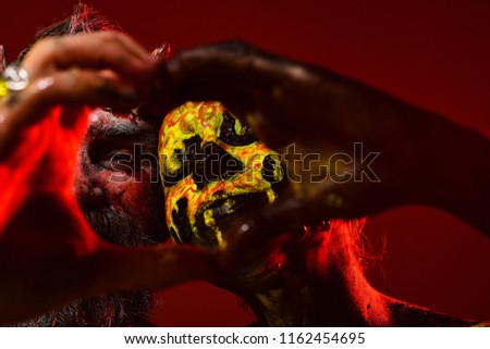 Halloween man and woman make heart hands. Couple in love on red background. Devil hipster with horns and girl skull makeup face. Valentines day, holidays, cosplay, celebration.